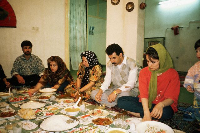 April 1997, Iran --- An Iranian family eats a meal in typical fashion. A carpet is spread onto the floor, the mother and father sit in the middle and the women serve the food. Shiraj, Iran | Location: Shiraj, Iran. --- Image by © Earl & Nazima Kowall/CORBIS