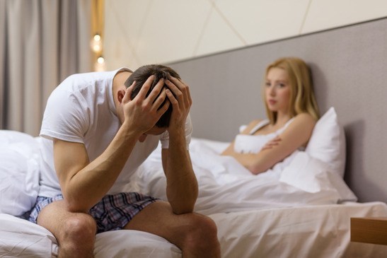 hotel, travel, relationships, and sexual problems concept - upset man sitting on the bed with woman on the back